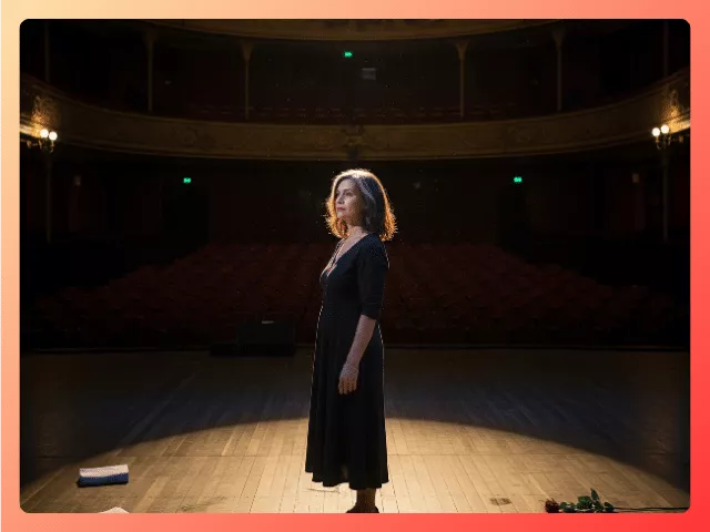 Woman standing alone on a dimly lit stage symbolizing a midlife identity shift and life transition after a major role change