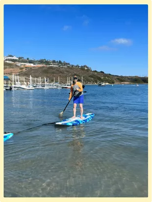 Midlife woman balancing on a stand-up paddleboard, smiling with confidence and joy as she tries something new.